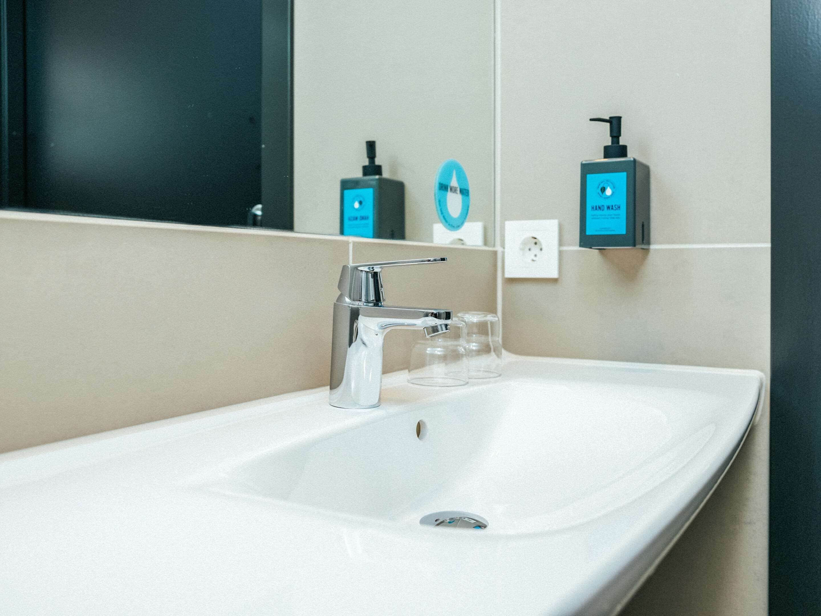 A modern bathroom with a white sink, chrome faucet, and two soap dispensers.