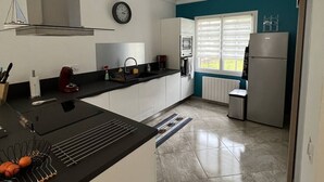 Una cocina moderna con encimera negra, armarios blancos, extractor de acero inoxidable y una ventana con persianas.