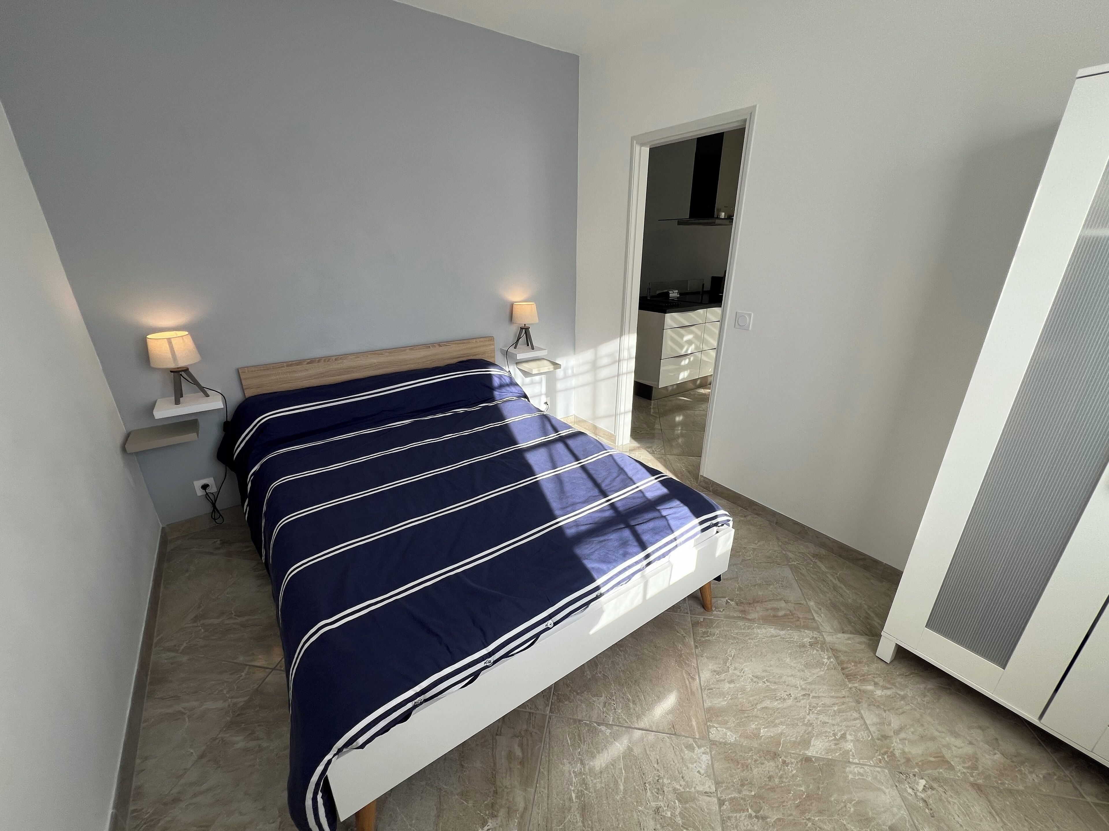Ein Schlafzimmer mit einem Bett, Nachttischlampen, einem Kleiderschrank und Blick in die Küche.
