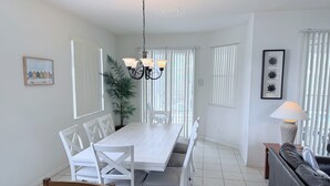 A dining area with a white table and chairs, a chandelier, a potted plant, and a sofa with a lamp. - Villa Hideaway with pool and gamesroom (Davenport)