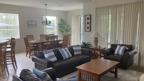 A spacious living room with a leather sofa, a wooden coffee table, and a dining area with a table and chairs. - Villa Hideaway with pool and gamesroom (Davenport)