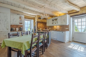 A rustic kitchen with wooden beams, a dining table with chairs, and a chandelier.
