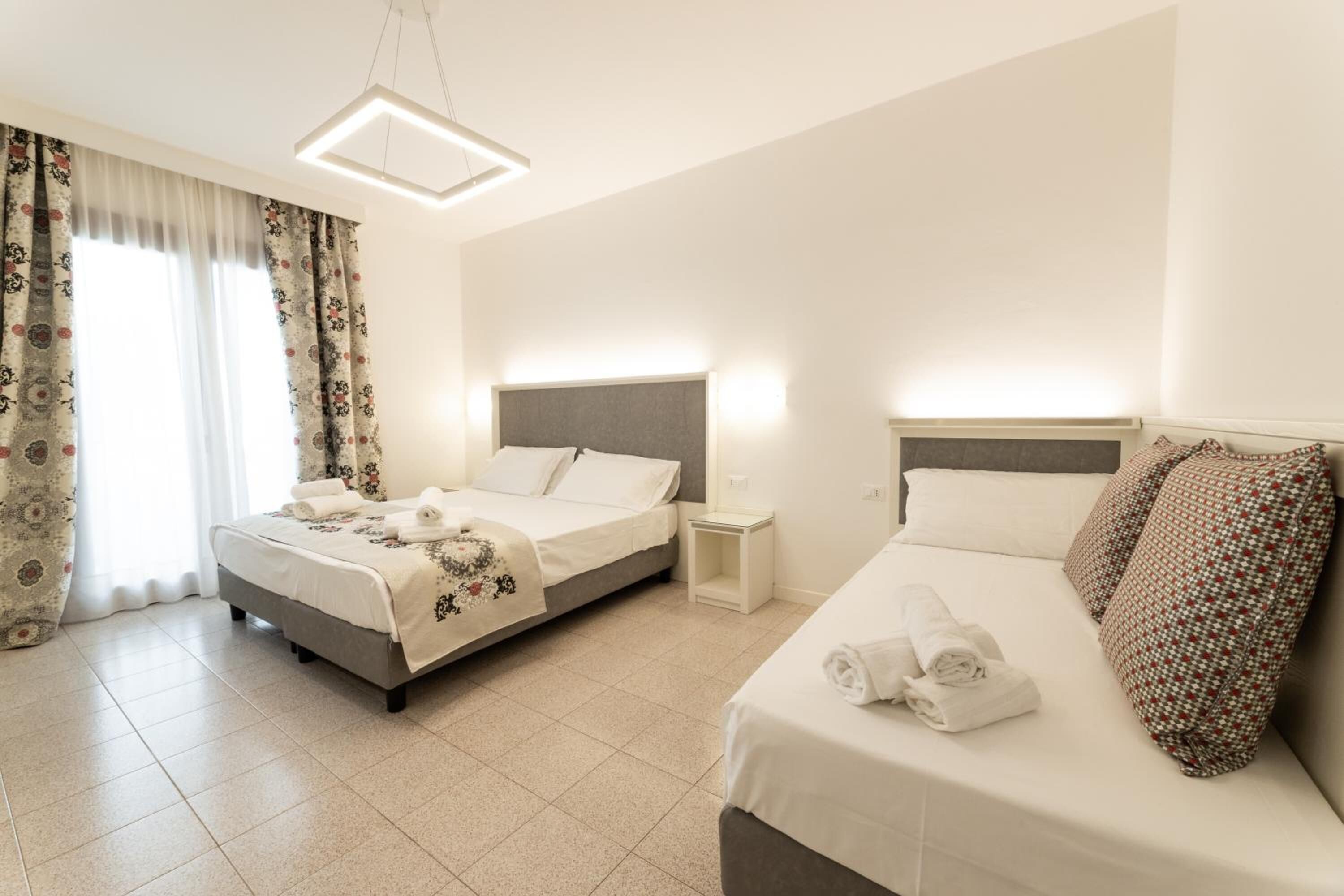 A hotel room with two beds, a bedside table, a nightstand, and a hanging light fixture.