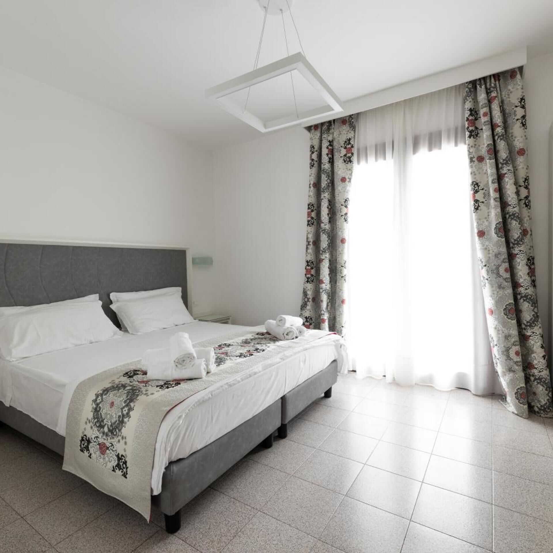 A modern hotel room with a large bed, a grey headboard, and floral curtains.