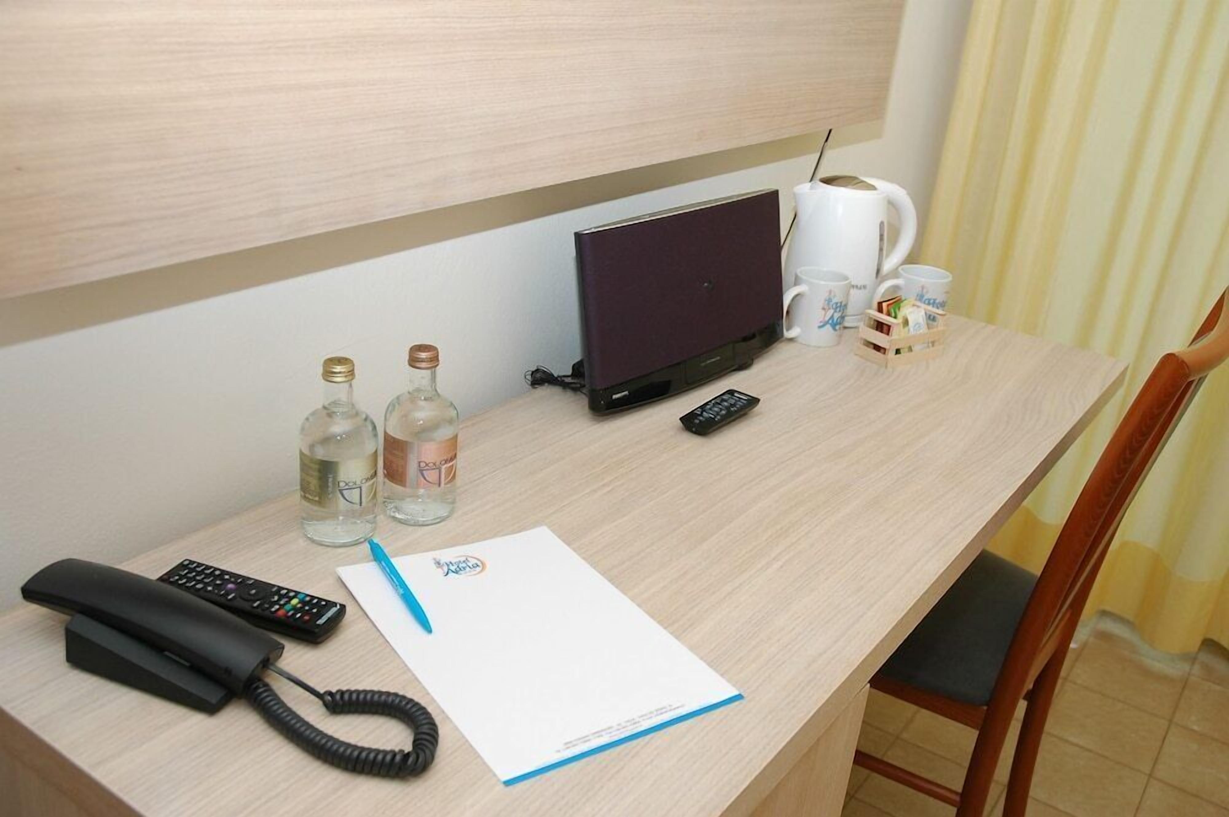 A hotel room desk with a laptop, a telephone, a remote control, a notepad, and two bottles of water.