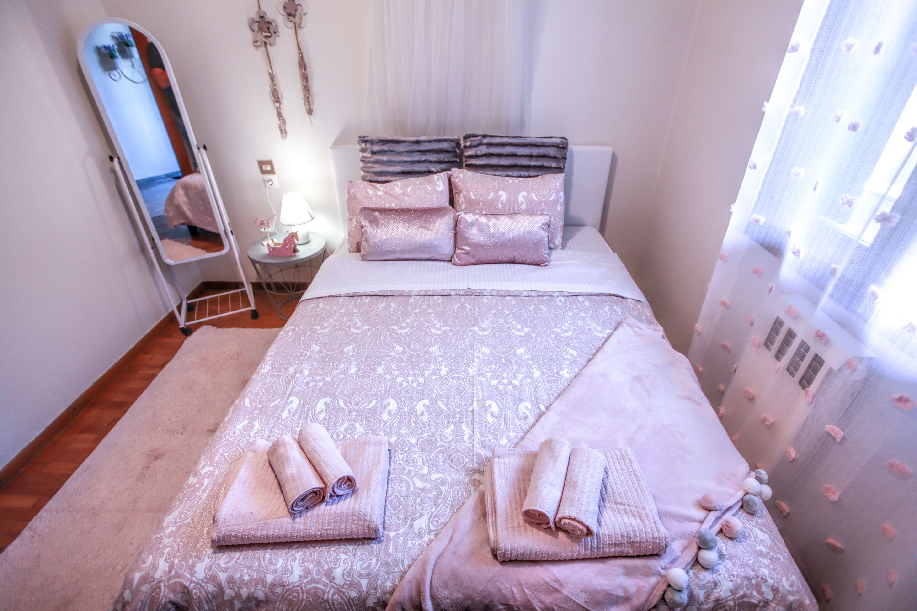 Un lit bien fait, avec une couvre-lit à motifs et des oreillers, une table de chevet avec une lampe et un miroir accroché au mur.