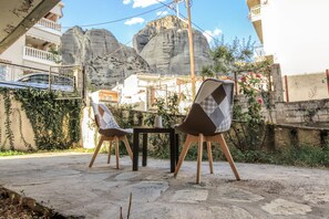 An outdoor seating area with a table and chairs, surrounded by a stone wall and vegetation. - Only yours Meteora (Kalabaka)