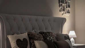 Een netjes opgemaakt bed met een beddekleed met een patroon en meerdere kussens, waaronder een hartvormig kussen.