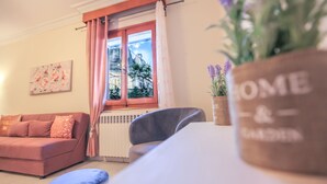Een woonkamer met een bank, een fauteuil, een tafel, een raam met gordijnen, een radiator en een 'HOME & SUGAR' bord.