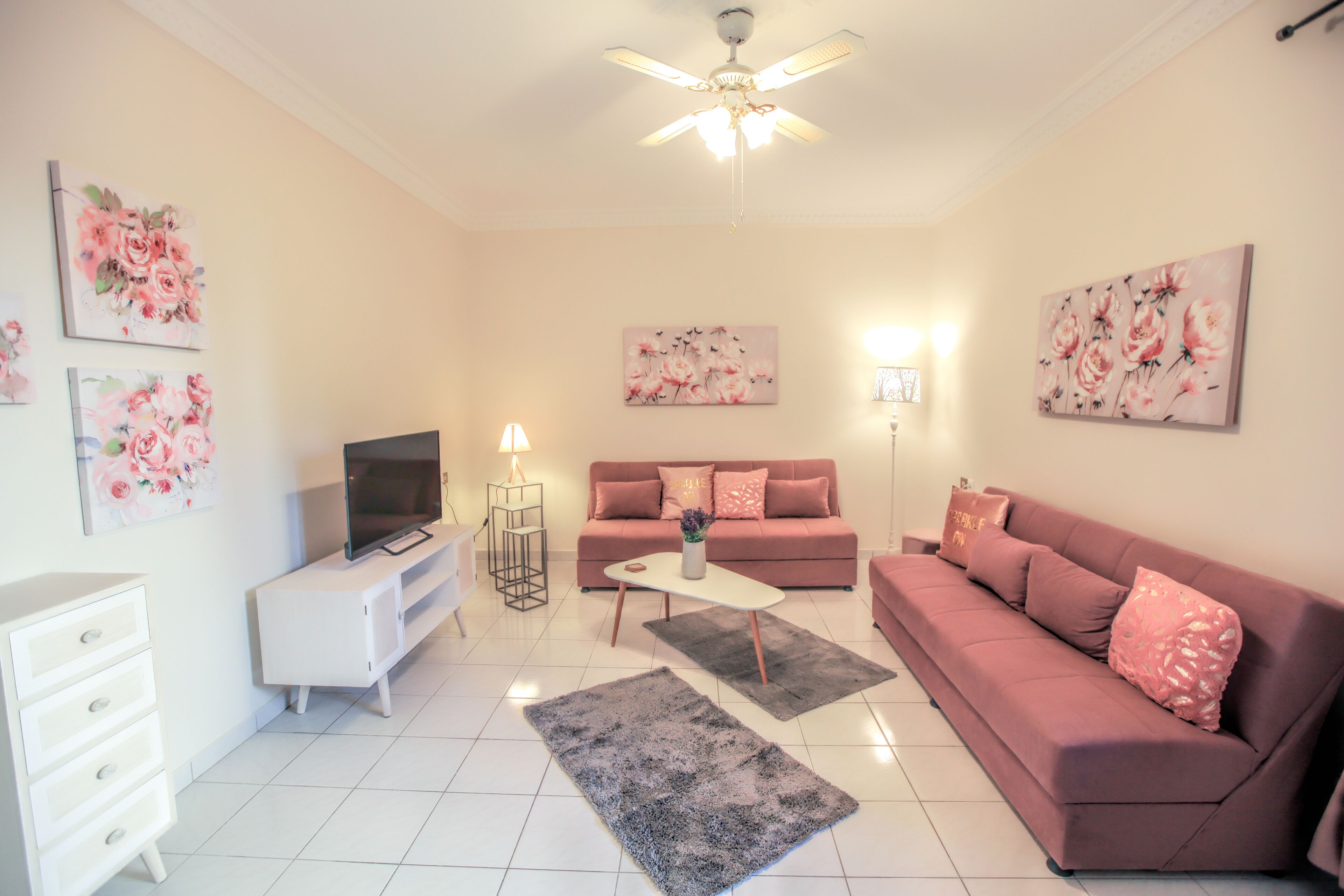 A modern living room with a flat-screen TV, a white coffee table, a pink sofa, and a grey rug.
