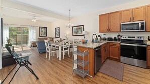 Una cocina moderna con armarios de madera, electrodomésticos de acero inoxidable y un comedor con mobiliario blanco.