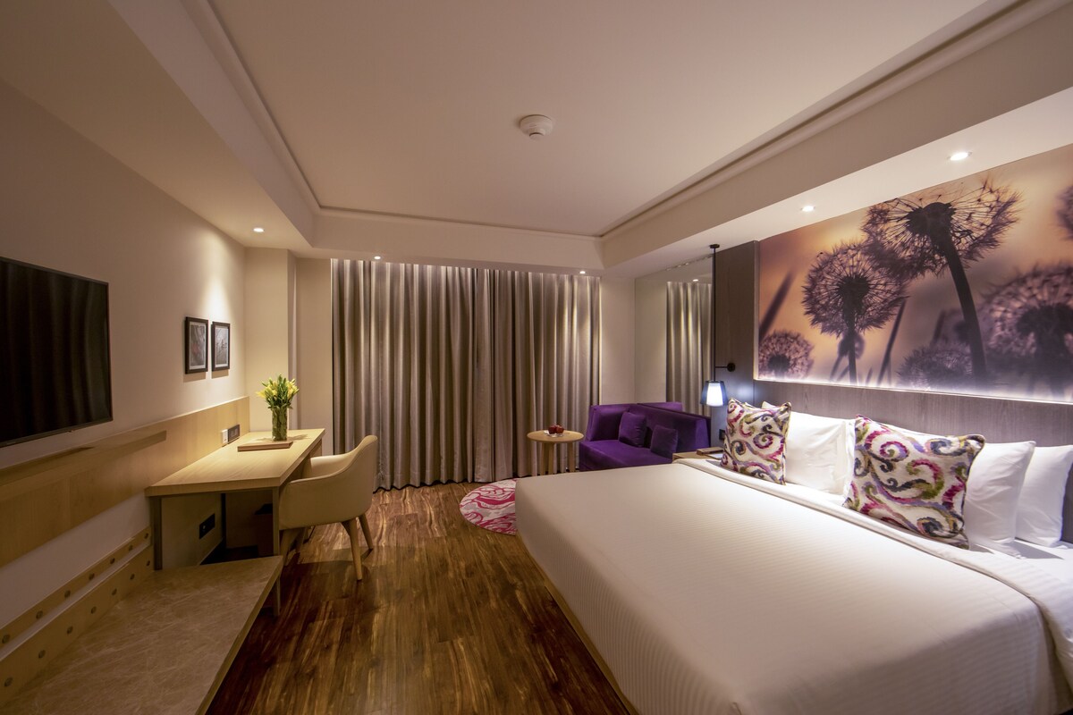A modern hotel room with a large bed, a desk, a chair, and a small table.