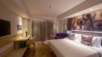 A modern hotel room with a large bed, a desk, a chair, and a small table.