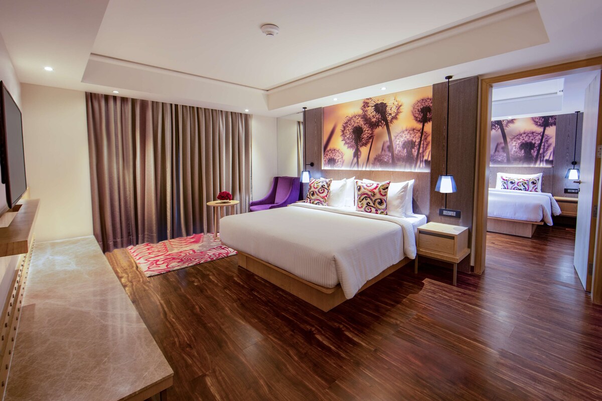 A modern hotel room with a large bed, a desk, and a view of another room.