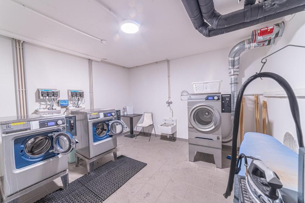 A laundry facility with multiple washing machines and dryers, a control panel, and a ventilation system.