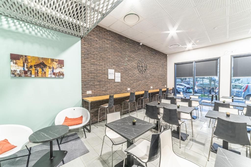 A modern dining area with tables and chairs, a brick wall with a clock, and a city view through large windows.