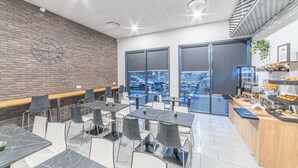 A modern cafe with marble-topped tables and chairs, a brick wall, and a view of the parking lot through large windows. - Montempô Bordeaux centre - Bassins à flot (Bordeaux)