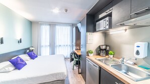 A modern hotel room with a bed, a small kitchenette, a dining area, and a view of the outdoors. - Montempô Bordeaux centre - Bassins à flot (Bordeaux)