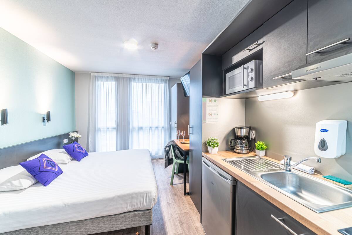 Een moderne hotelkamer met een bed, een kitchenette, een eethoek en uitzicht op het omliggende landschap.