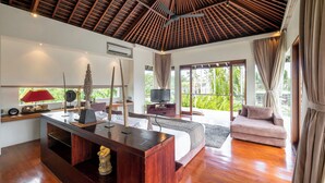 A spacious room with a wooden ceiling, a bed, a sofa, a TV, and a desk with decorative items. - Villa Kalyani (Canggu)
