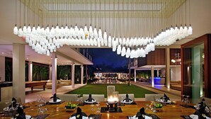 A modern dining area with a long table set for a meal, a pool in the background, and a unique ceiling light fixture. - Villa Kalyani (Canggu)