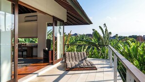 A balcony with a cushioned seating area, a wooden table, and a television. - Villa Kalyani (Canggu)