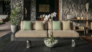 A modern living room with a beige sofa, green cushions, and a central orchid plant. There are two decorative lanterns on the coffee table. - Villa Mana by Elite Havens (Canggu)