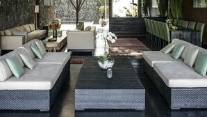 A modern living room with a stone wall, two sofas, a coffee table, and a dining area with chairs. - Villa Mana by Elite Havens (Canggu)