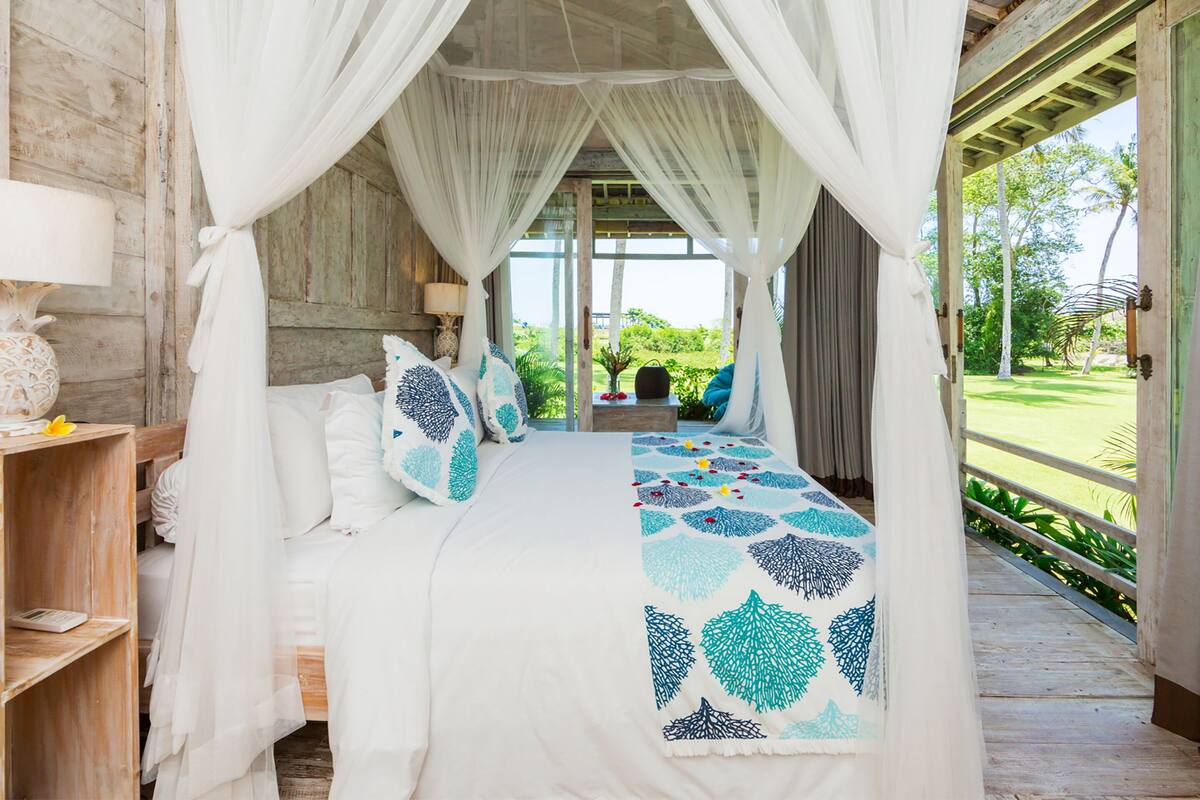 A bedroom with a canopy bed, wooden walls, and a view of the garden.