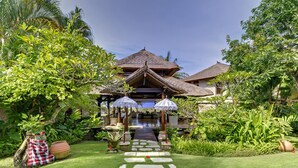 A traditional-style villa with a thatched roof, a stone pathway leading to the entrance, and lush tropical vegetation surrounding the property.