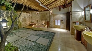 A bathroom with a stone wall, a bathtub, a sink, and a mirror.