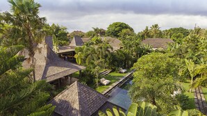 A tropical resort with thatched-roof buildings, a swimming pool, and lush greenery. - Villa Zelie (Canggu)