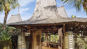 A traditional wooden structure with a thatched roof, surrounded by lush greenery and palm trees. - Villa Zelie (Canggu)