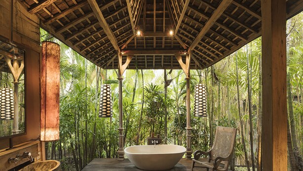 A wooden deck with a large bathtub, a rocking chair, and a rustic wooden bench. - Villa Zelie (Canggu)