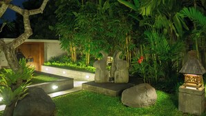 Um jardim com esculturas de pedra, um caminho bem iluminado e vegetação exuberante.