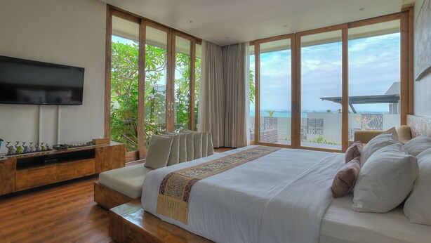 Um quarto com uma cama grande, televisão e vista para o mar.