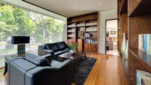 Uma sala de estar moderna com um sofá de couro preto, uma mesa de centro e uma estante repleta de livros.