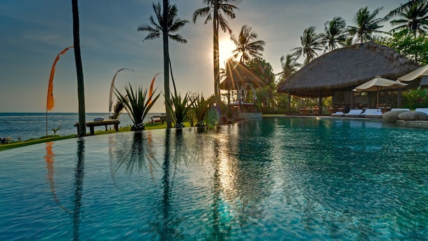 A pool with clear water, surrounded by palm trees and a thatched-roof structure. - Taman Ahimsa by Elite Havens (Cemagi)