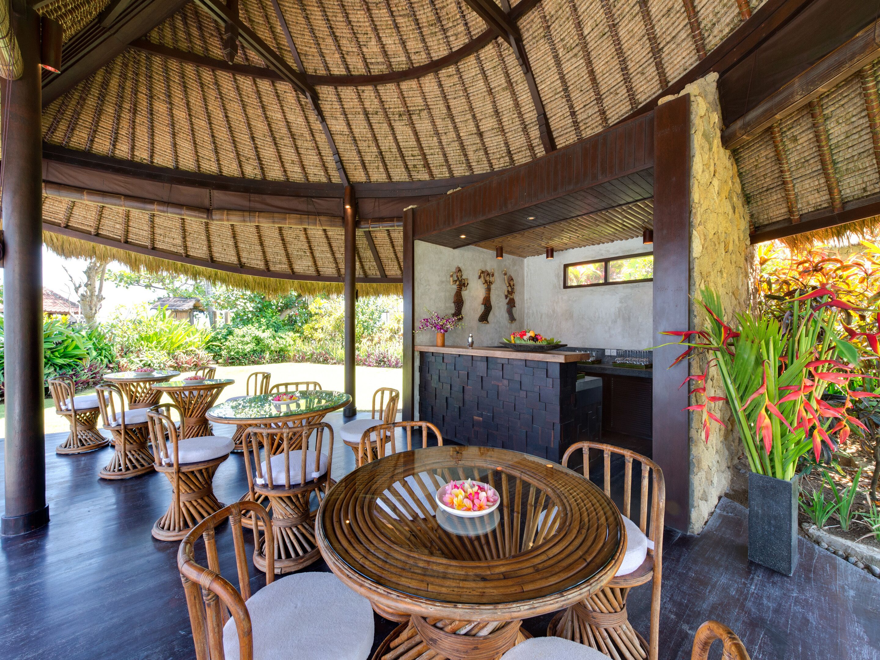 Un área de comedor al aire libre con mobiliario de mimbre y techo de paja.