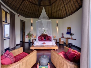 A spacious room with a bed under a canopy, wicker furniture, and a wooden floor.
