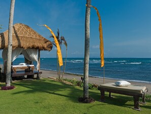 A beachside resort with a thatched-roof hut, a lounge area with a bench, and a view of the ocean.