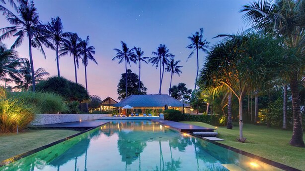 A swimming pool with a clear view of the surrounding landscape, including palm trees and a building with a covered area. - Villa Samadhana (Sukawati)