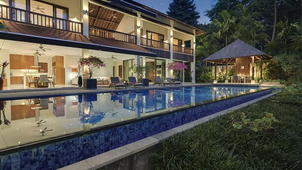 Una casa moderna de dos pisos con piscina, mobiliario exterior y un patio cubierto.