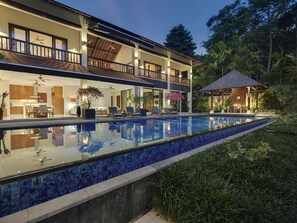 Ein modernes, zweistöckiges Haus mit Swimmingpool, Sitzgelegenheit im Freien und einer überdachten Terrasse.