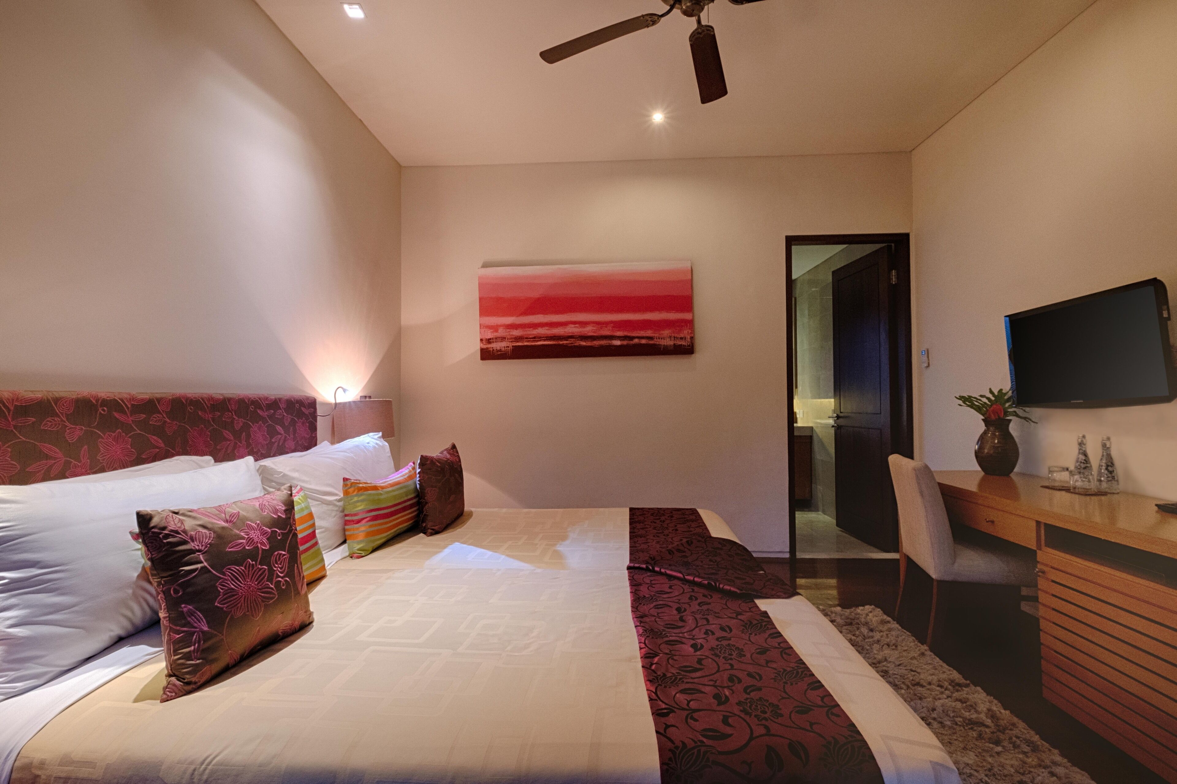 A modern bedroom with a large bed, a desk, and a TV.