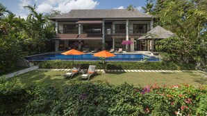 Una casa de dos pisos con piscina, rodeada de vegetación exuberante y un jardín bien cuidado.