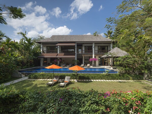 Ein zweistöckiges Haus mit Swimmingpool, umgeben von üppiger Vegetation und einem gepflegten Garten.