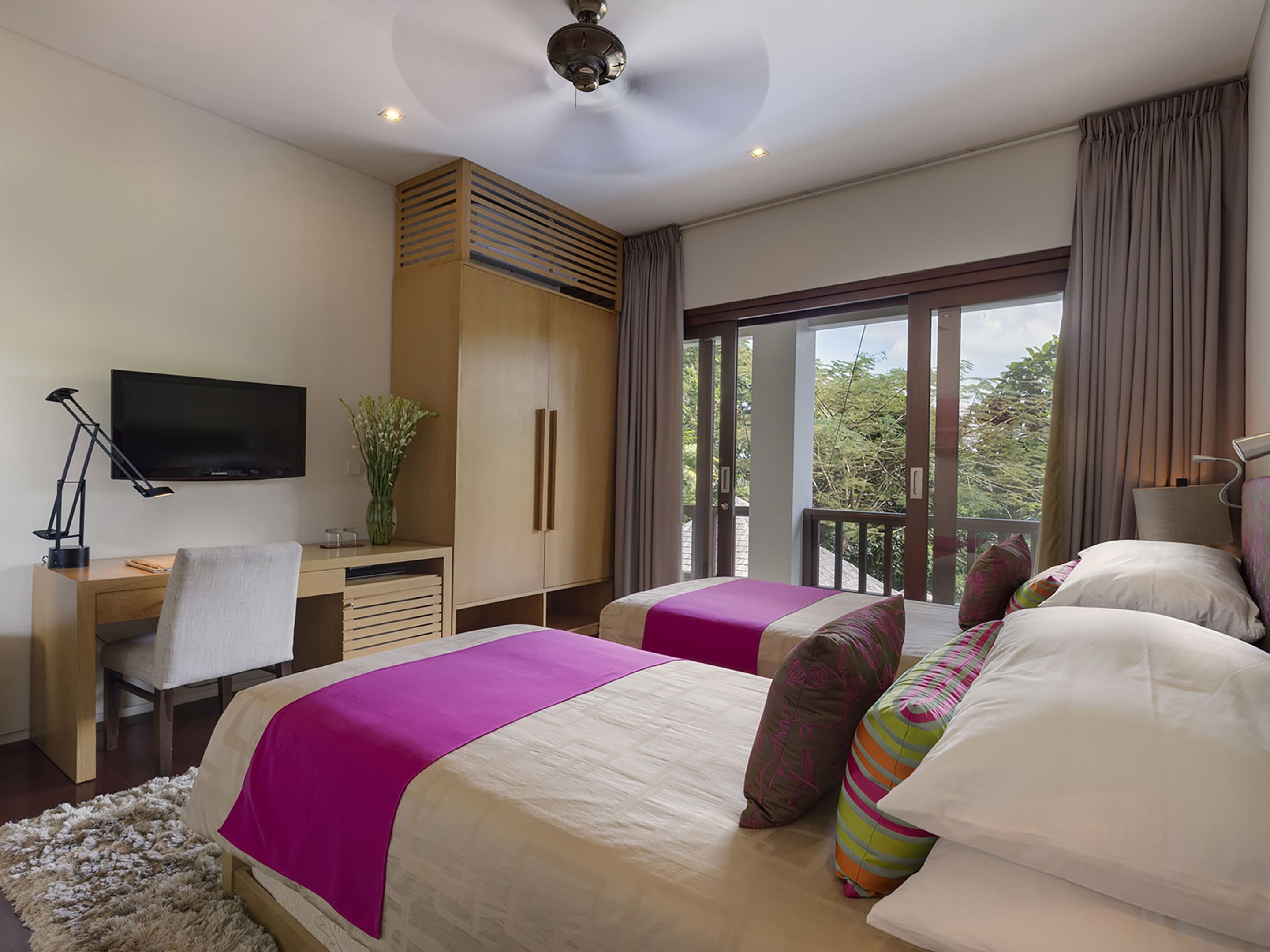 Habitación de hotel con dos camas, un escritorio con televisor, una silla y un balcón con vistas.