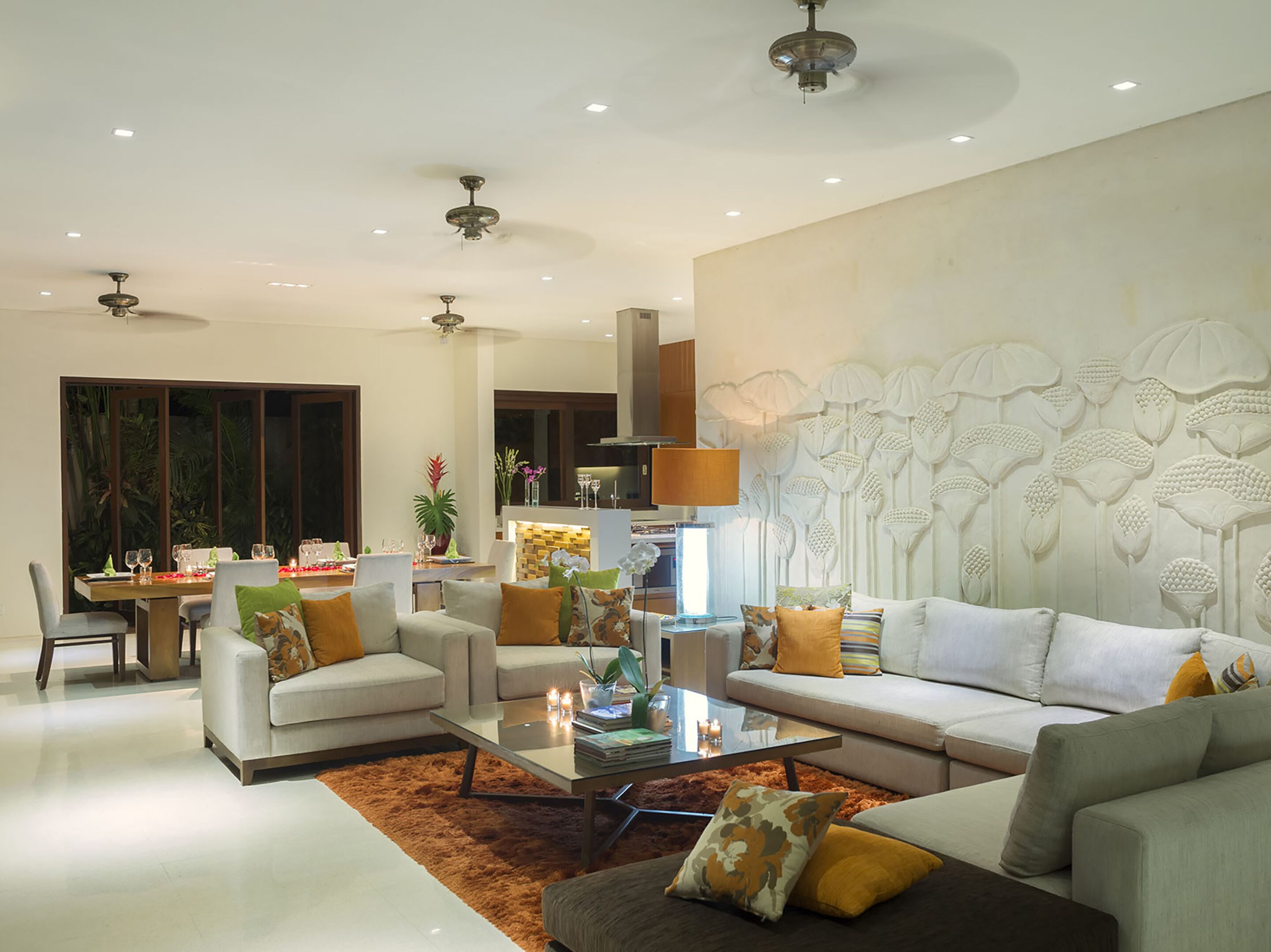 A modern living room with a sofa, armchairs, a coffee table, and a dining area with a table set for two.