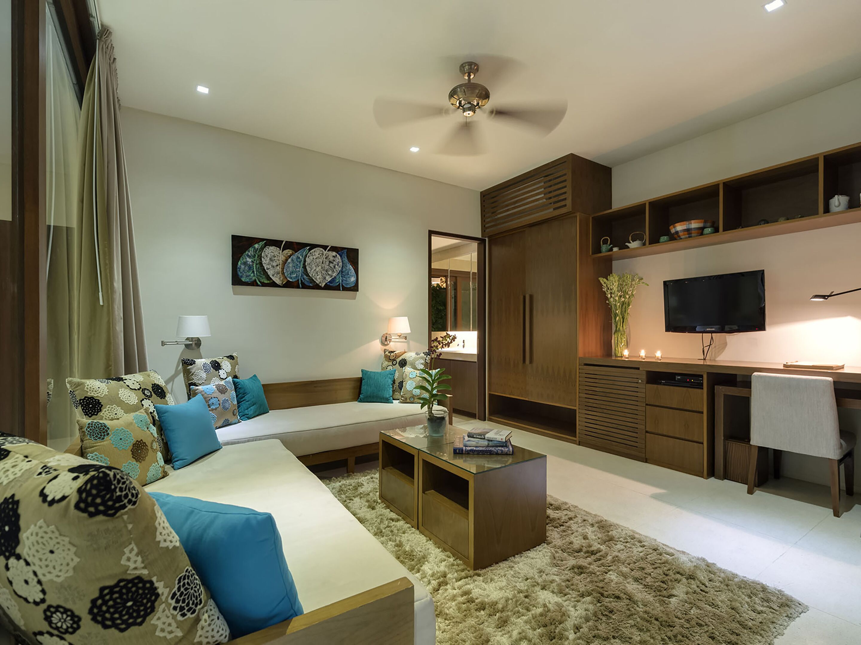 A modern living room with a sofa, coffee table, and TV. There is a wooden cabinet and a ceiling fan.